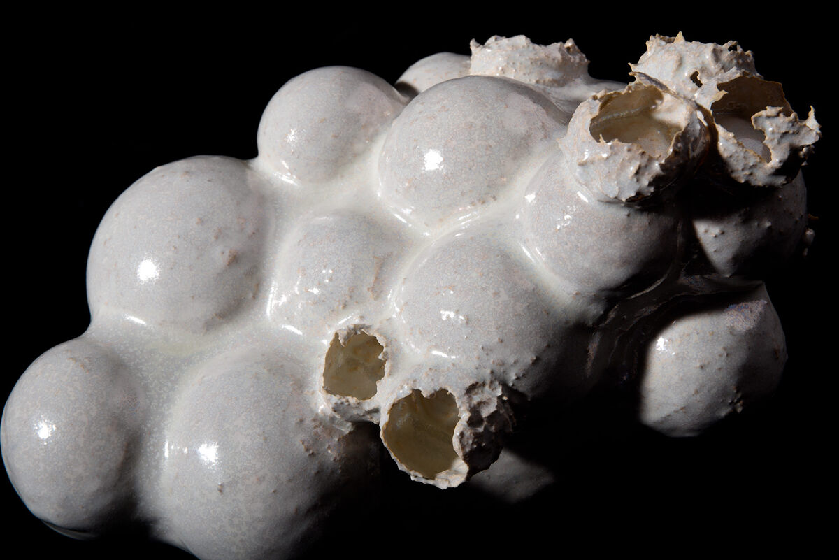 Ceramic sculpture of several egg-like forms that show several broken glazed egg shells on the top, photographed on a black background